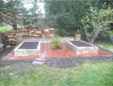 Retaining wall beside a paved patio in a Chicago-area yard, where the base course meets grade before winter frost heave