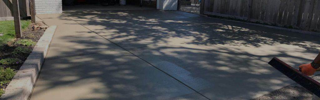 Freshly poured concrete driveway being broom-finished beside a wood fence in a Chicago yard