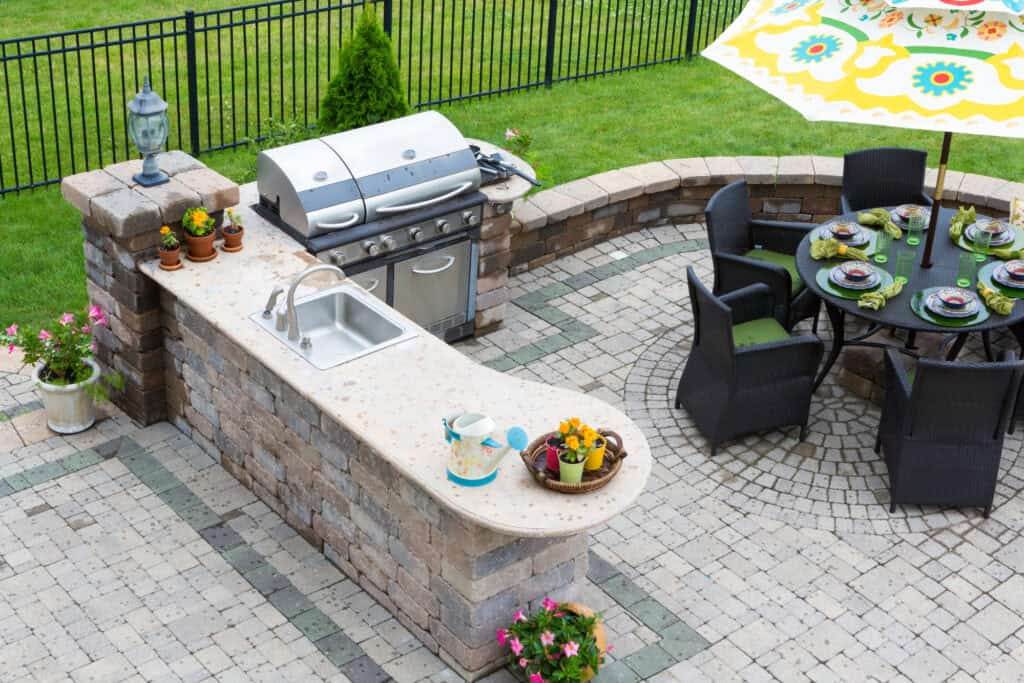 Outdoor kitchen and dining table on a paved patio, the setting a shade structure covers