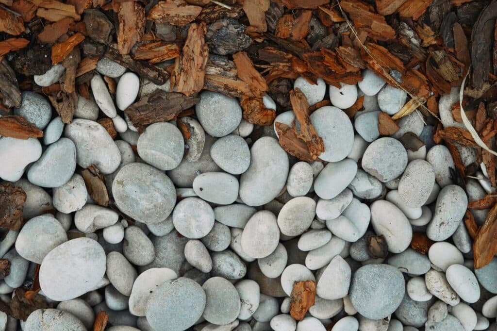 Smooth stone mulch pebbles beside shredded bark mulch chips, showing the texture contrast clearly
