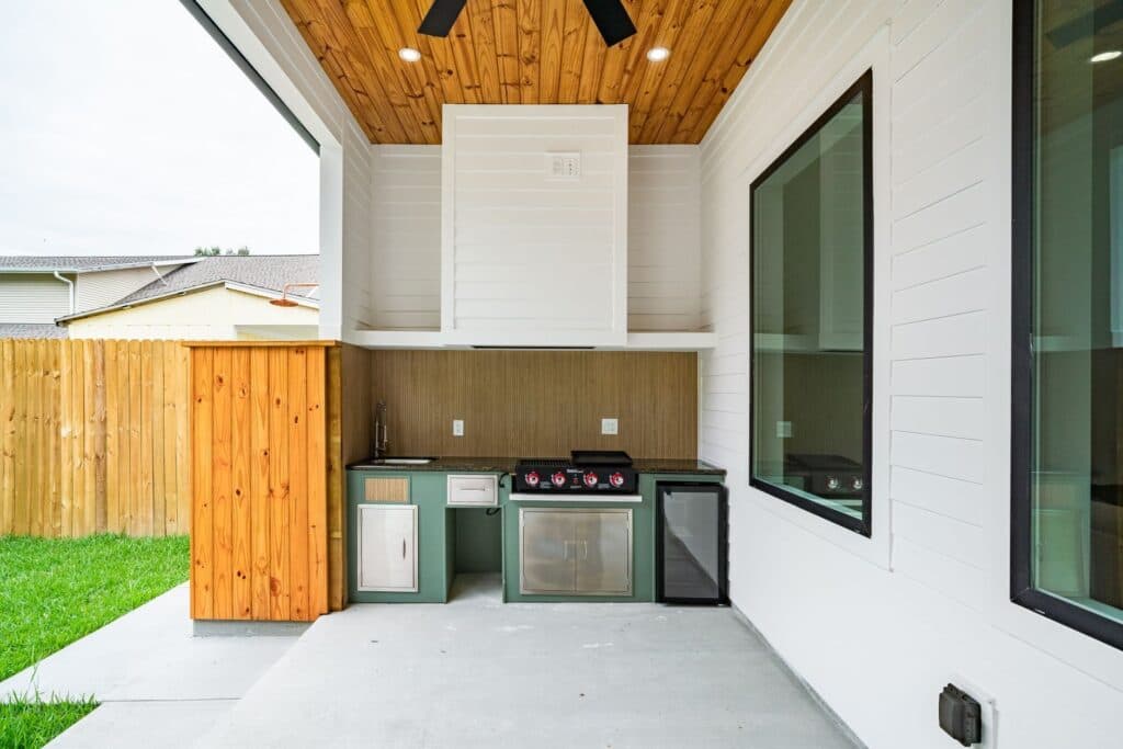 Built-in outdoor kitchen with grill, sink and cabinets under a covered backyard patio