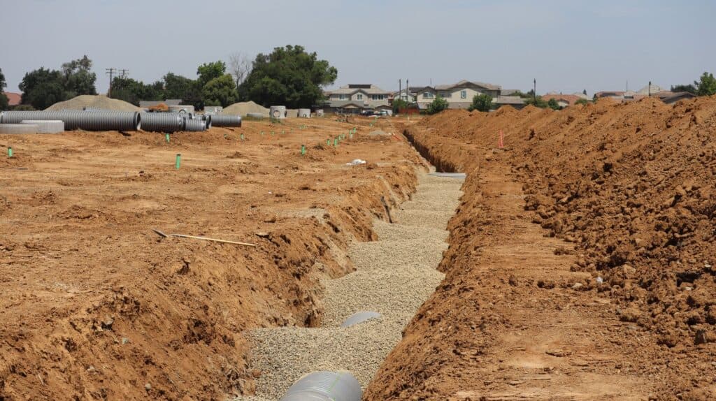 Wide view of a drainage trench and pipes being installed in a residential Chicago-area yard with heavy clay soil