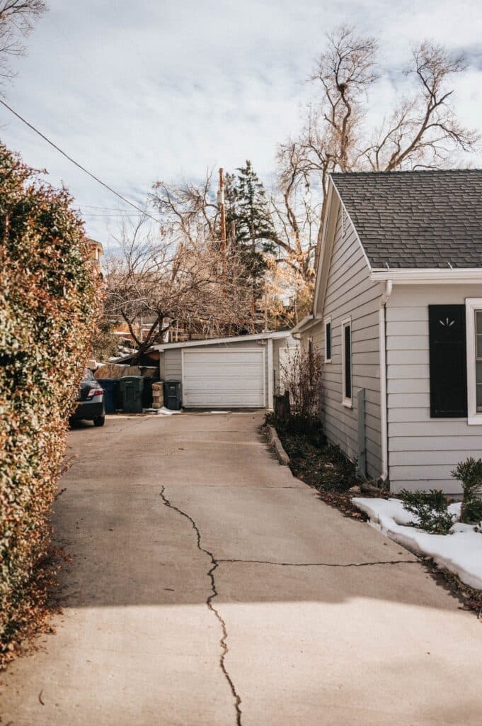 Concrete driveway with a long surface crack running toward a garage in a wintry Chicago yard