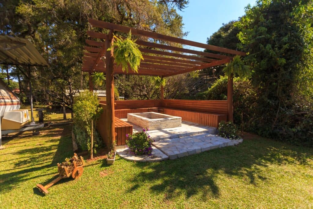 Freestanding wood pergola over a stone patio and fire pit in an open backyard lawn