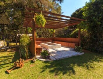 Freestanding wood pergola over a stone patio and fire pit in an open backyard lawn