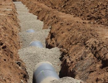 Open French drain trench with perforated pipe bedded in washed gravel, R & G Almanza drain installation Chicago
