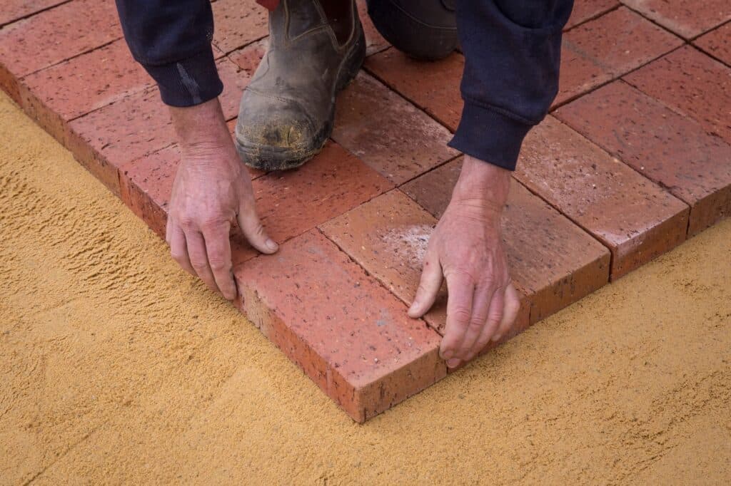 Crew hand-setting brick pavers into a compacted sand base, R&G Almanza paver patio installation