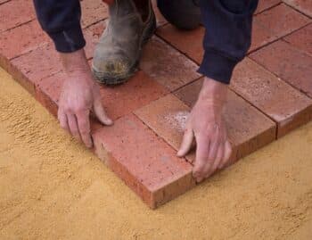 Crew hand-setting brick pavers into a compacted sand base, R&G Almanza paver patio installation