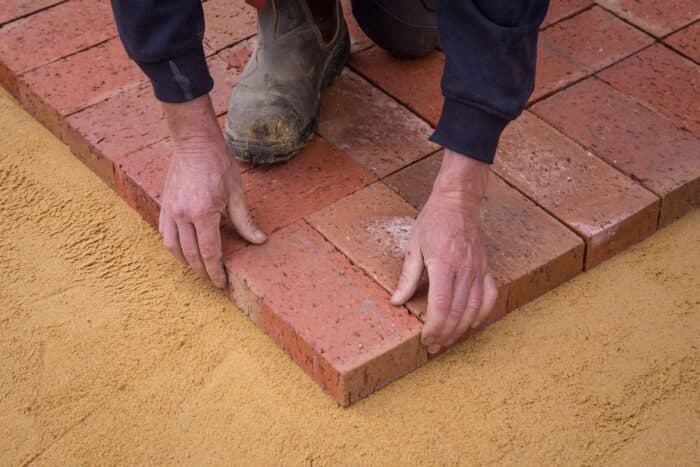 Crew hand-setting brick pavers into a compacted sand base, R&G Almanza paver patio installation
