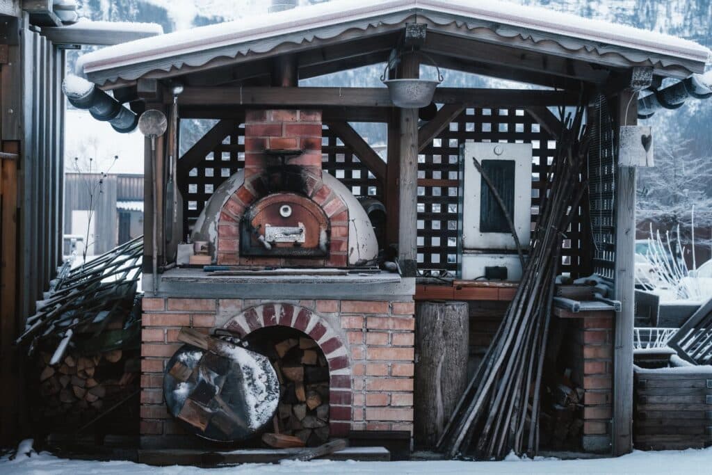 Brick masonry pizza oven with a wood storage nook, built as part of an outdoor kitchen